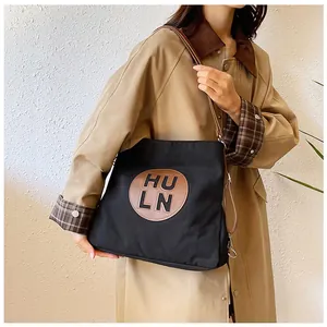 Detail of black canvas tote bag with brown leather handles and HU LN patch logo