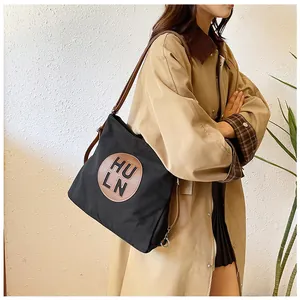 Close-up of black nylon tote bag with brown leather HULN logo patch and shoulder strap
