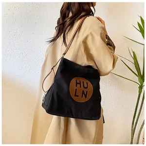 Detail of black canvas tote bag showing brown leather patch and high-quality silver hardware