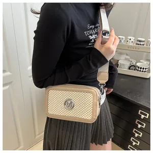 Close-up of beige woven crossbody bag featuring a round M metal buckle and wide strap