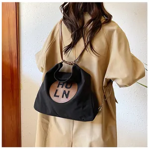 Detail of black canvas tote bag featuring brown leather HULN patch and slender shoulder straps