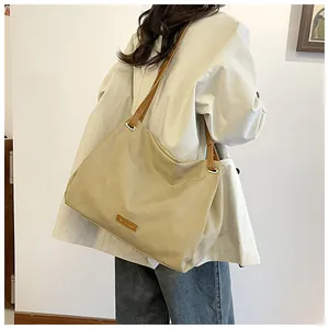 Detail view of a large khaki tote bag with brown leather straps and metal rings
