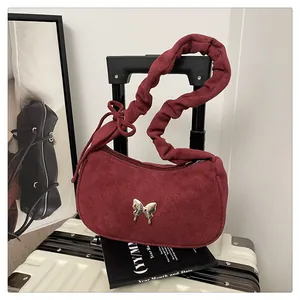 Detailed close-up of dark red suede handbag featuring a metal butterfly buckle and ruched strap