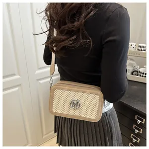Close-up of beige woven crossbody bag with silver M logo and wide canvas shoulder strap