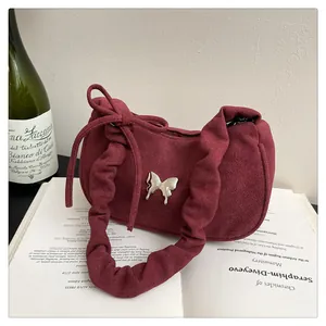 Close-up of a burgundy suede shoulder bag with silver butterfly and pleated strap