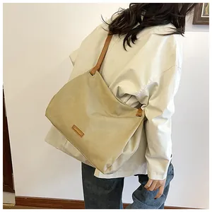 Detail of a large beige tote bag with brown straps worn over a model's shoulder