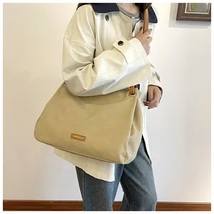 Detail of khaki tote bag featuring gold logo plate and brown contrasting shoulder strap