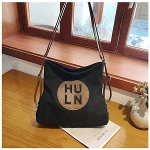 Detail of a black canvas tote with brown straps and HULN logo on a wooden surface