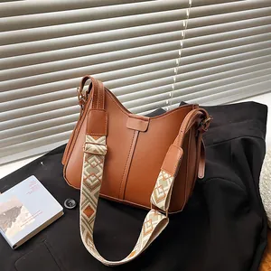 Caramel brown crescent shoulder bag with wide geometric patterned strap and gold hardware
