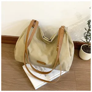 Detail of beige canvas tote bag with brown leather straps and metallic logo plate