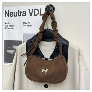 Close-up of brown suede shoulder bag featuring a gold butterfly buckle and pleated strap