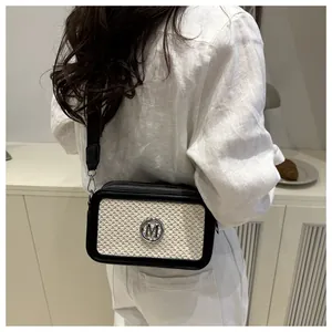 Detail of crossbody bag with woven texture, metal M logo, and wide shoulder strap on model
