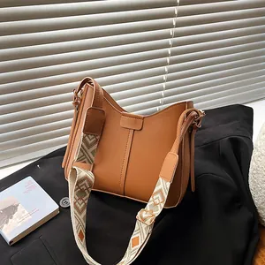 Brown leather tote bag with a colorful geometric wide shoulder strap on a black blazer