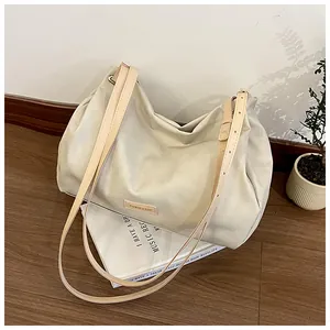Close-up of beige large tote bag with adjustable leather strap on books with greenery
