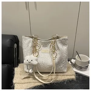 Detail of white pleated tote bag with golden chain handle and cloud plush charm