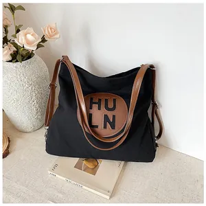Detail of black canvas tote bag showing brown leather strap and adjustable metal buckle