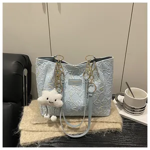 Detail of light blue tote bag featuring golden chain straps and white cloud plush charm