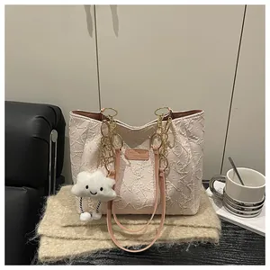 Close-up of cream tote bag featuring textured fabric and gold metal chain strap with plush charm