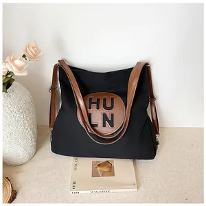 Detail of black canvas tote with HULN leather patch on textured light surface