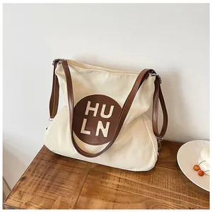 Detail view of canvas tote bag with brown leather straps and HU LN logo on a wooden table