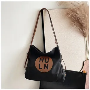 Detail of black canvas tote bag with brown leather patch and adjustable shoulder straps