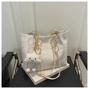 Detail of white textured tote bag featuring gold ring handles and cloud plush charm