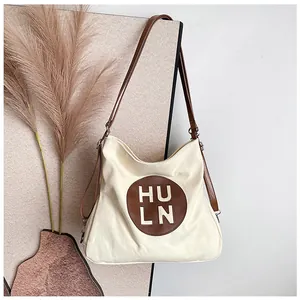 Detailed view of off-white canvas hobo bag with brown leather patch and shoulder strap