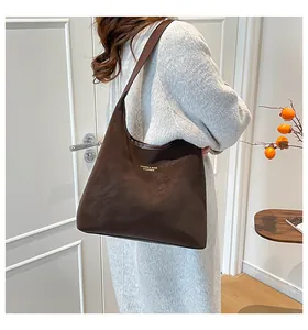 Detail view of large dark brown suede tote bag with golden logo on model's shoulder