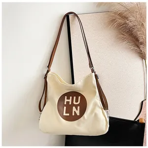 Detail of canvas tote bag with brown leather HU LN patch and matching shoulder straps