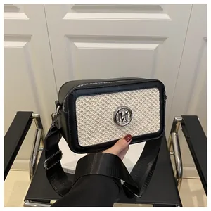 Detail view of woven leather crossbody bag with silver M logo and wide strap