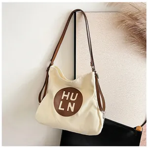 Detail of adjustable brown strap and logo patch on the minimalist beige canvas tote bag