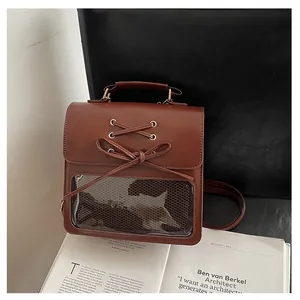 Detail of a brown ita bag featuring a clear window, lace-up bow, and golden hardware