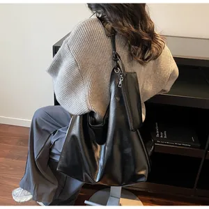 Detail of a black leather tote bag with a matching small zipper pouch on a shoulder strap