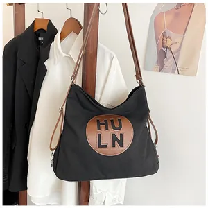 Detail of black canvas tote bag with brown leather patch and adjustable strap