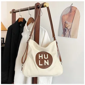 Detail of canvas hobo bag with brown leather straps and HU LN logo on wood hanger