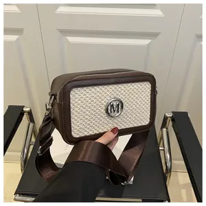 Close-up of contrast crossbody bag with silver M logo and wide brown shoulder strap