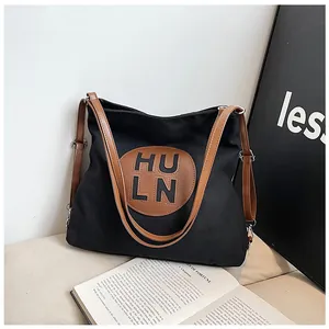 Detail of black canvas shoulder bag with brown leather patch and silver buckle