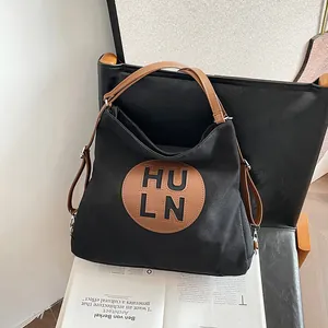 Black canvas tote bag with brown leather straps and HULN logo on a stylish leather chair