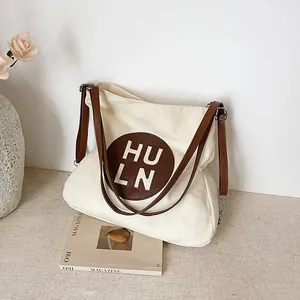 Minimalist beige canvas tote bag with brown leather straps and circular logo patch