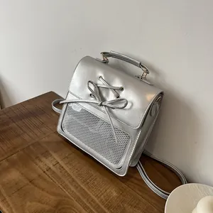Silver metallic minimalist backpack with bow detail and mesh window on wooden bench