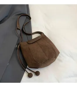 Close-up of brown suede bucket bag with drawstring details and sphere charms