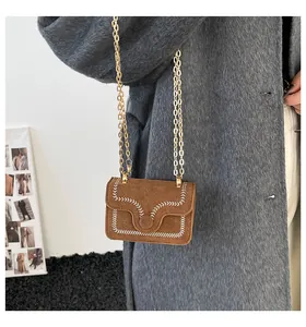 Detail der braunen Wildledertasche mit weißer Wellennaht und goldener Kette