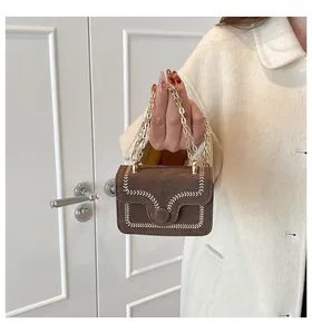 Detail einer braunen Wildleder-Mini-Handtasche mit beiger Naht und Goldkettenriemen
