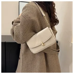 Detail of a beige shoulder bag with a unique golden peanut-shaped clasp and chain strap