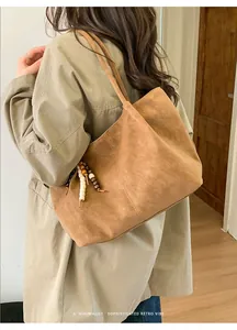 Detail of camel suede tote bag featuring a decorative beaded charm and long shoulder straps