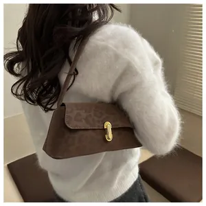 Detail of dark brown leopard print suede underarm bag with gold metal buckle on white sweater