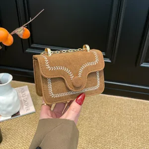 Braune Wildleder-Umhängetasche mit Stickerei und Goldkette in der Hand gehalten präsentiert