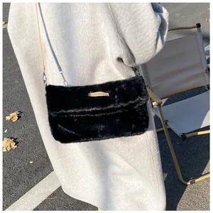 Detail of a black plush crossbody bag with leather brand tag and silver metal hooks