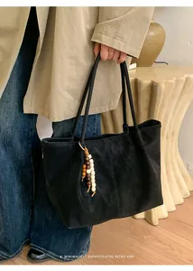 Close-up of black suede tote bag with wooden bead charm and minimalist retro design