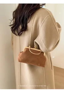 Schicke Retro Wildledertasche in Braun mit goldenem Griff auf einem beigen Mantel